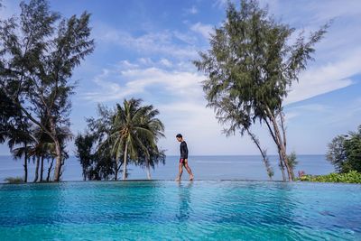 Side view of man walking on poolside by sea against sky