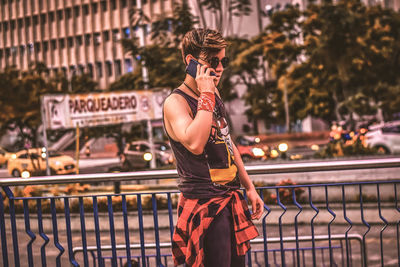 Young woman wearing sunglasses standing against railing in city
