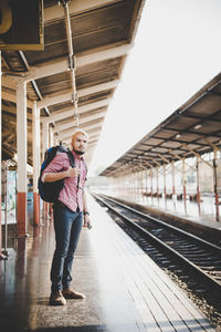 Full length portrait of young man standing at railroad station platform