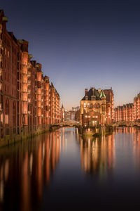 Illuminated buildings by river against sky in city at night