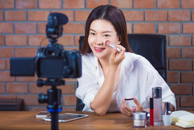 Portrait of smiling young woman holding camera on table