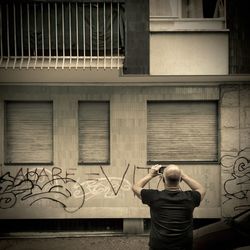 Rear view of man photographing against building