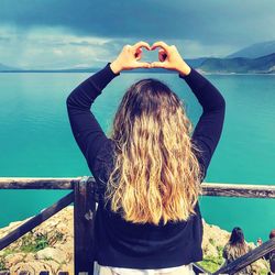 Rear view of woman photographing by lake against sky