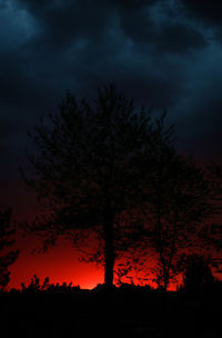 Silhouette trees against dramatic sky at sunset
