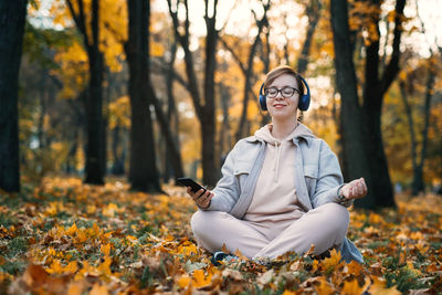 Caucasian middle aged woman in earphones listening to music, meditation app on smartphone and