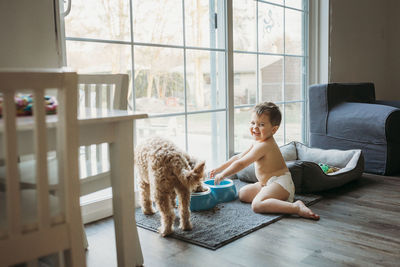 Toddler boy in diaper playing with dog's water dish in living room