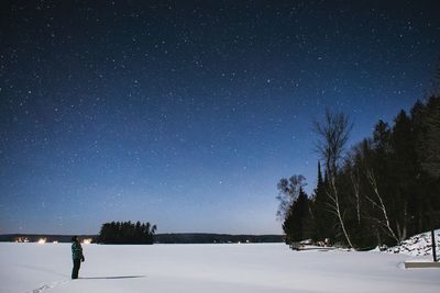 Side view of person standing on snow covered field against star field