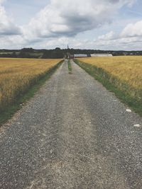 Dirt road amidst field against sky