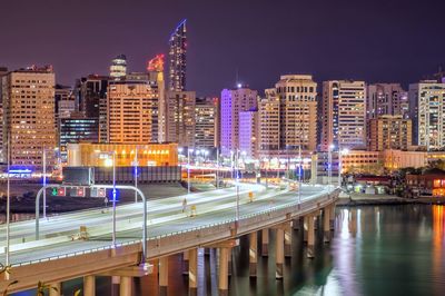 Illuminated buildings by river against sky in city at night