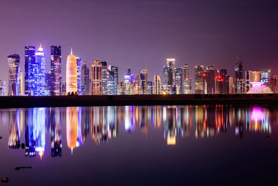 Illuminated buildings by river against sky at night
