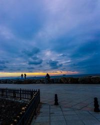 People on railing against sky at sunset