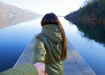 Cropped image of man holding girlfriend hand on jetty over river