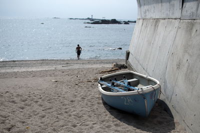 Moored boat with shirtless man walking at beach by sea against sky