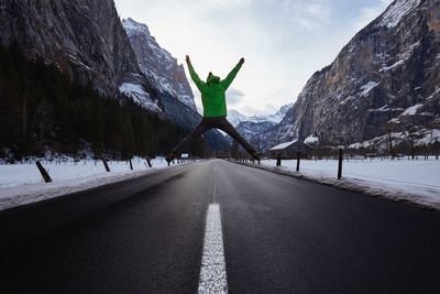 Rear view of man jumping on road by snowcapped mountain