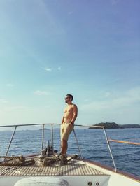 Shirtless man standing on boat sailing in sea against sky