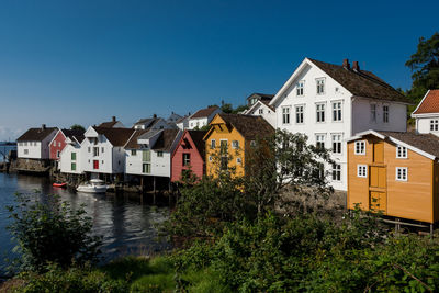 Houses by river and buildings against blue sky