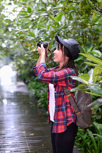 Woman photographing through camera against tree