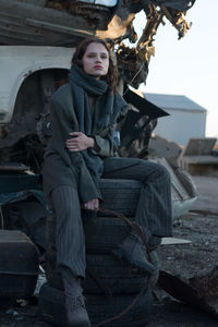 Thoughtful young woman sitting on stacked tire at junkyard