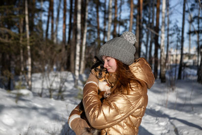 A young girl in the forest in winter holds a dog in her arms and enjoys the weather 