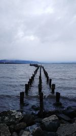 Wooden posts in sea against sky