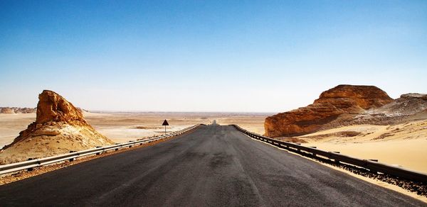 Road leading towards mountains against clear sky