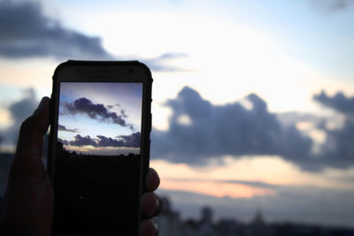 Close-up of hand holding smart phone against sky