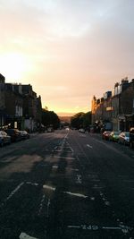 City street by buildings against sky during sunset