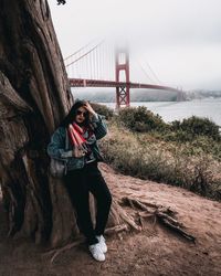 Portrait of young woman standing on bridge against sky
