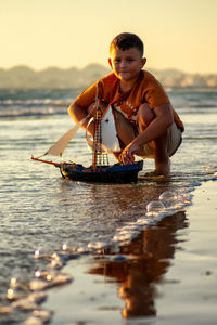 Portrait of boy playing with a boat against sky during sunset