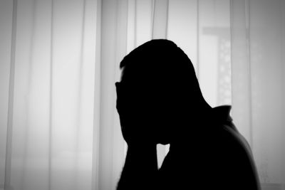 Portrait of silhouette woman standing against window at home