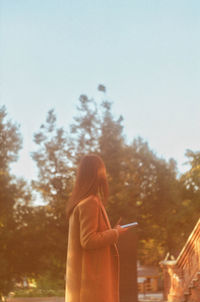 Rear view of woman standing by trees against sky