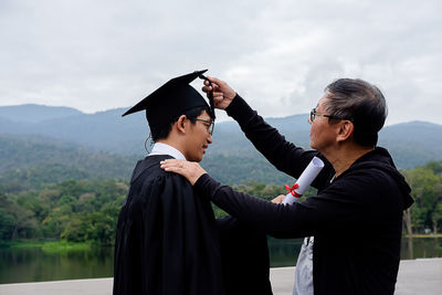 Father touching mortarboard of graduate son outdoors