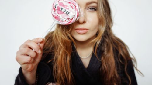 Portrait of young woman holding candy against white background