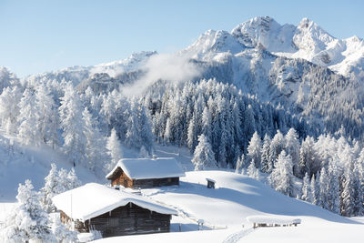 Winter mountain landscape with snowy forest and traditional alpine chalet
