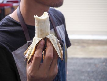 Midsection of mid adult man eating banana while standing on street