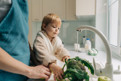 Little cute toddler daughter helps mom to wash vegetables in the kitchen in the sink.