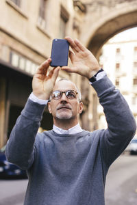 Man photographing with smart phone while standing in city