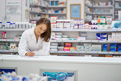 Pharmacist writing in note pad at pharmacy