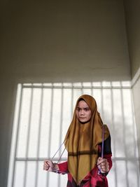 Young woman looking away while standing against wall