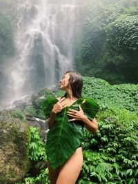 Woman holding a big leaf near a waterfall in the jungle