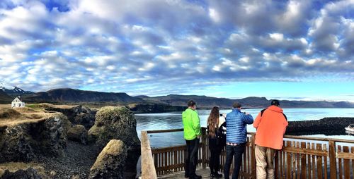 Rear view of men overlooking calm lake against cloudy sky