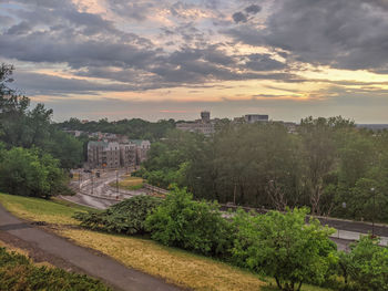 Trees in city against cloudy sky