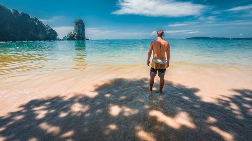 Rear view of shirtless man standing at beach against sky