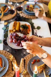 From above of crop anonymous female in wristwatch taking tasty grapes at table during christmas dinner