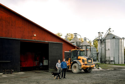 Mature farmers with dog standing outside dairy factory