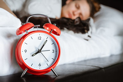  woman sleeping with pet cat on white blanket bed cozy at home in bedroom. close up of alarm clock