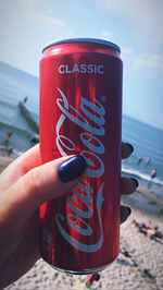 Close-up of hand holding drink at beach against sky