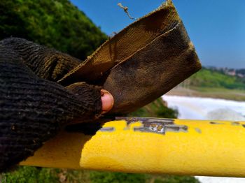 Close-up of hand holding yellow leaf against sky