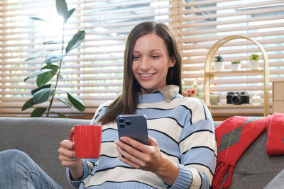 Young woman using mobile phone while sitting at home