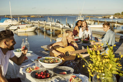 Friends listening to woman playing guitar in party at harbor